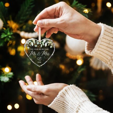 Heart-shaped glass ornament featuring "The Year We Became Mr & Mrs - 2026" in a navy blue gift box with an ivory ribbon.