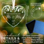 Heart-shaped glass ornament featuring "The Year We Became Mr & Mrs - 2026" in a navy blue gift box with an ivory ribbon.
