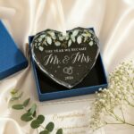 Heart-shaped glass ornament featuring "The Year We Became Mr & Mrs - 2026" in a navy blue gift box with an ivory ribbon.