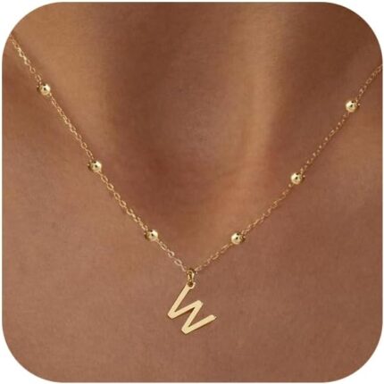 Close-up of a delicate 14K gold-plated initial 'W' necklace on a simple bead chain, worn by a woman.