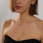 Close-up of a delicate 14K gold-plated initial 'W' necklace on a simple bead chain, worn by a woman.