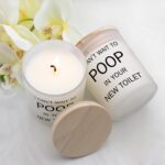 Frosted white jar candle with humorous text "I CAN'T WAIT TO POOP IN YOUR NEW TOILET" and a lit wick, on a neutral background