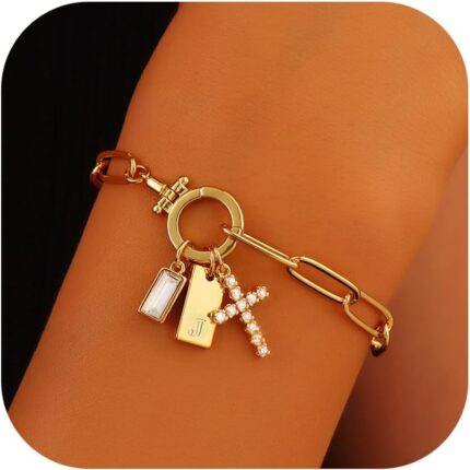Close-up of a gold-plated paperclip link chain bracelet with a letter J initial charm and a small cross charm, on a light bac